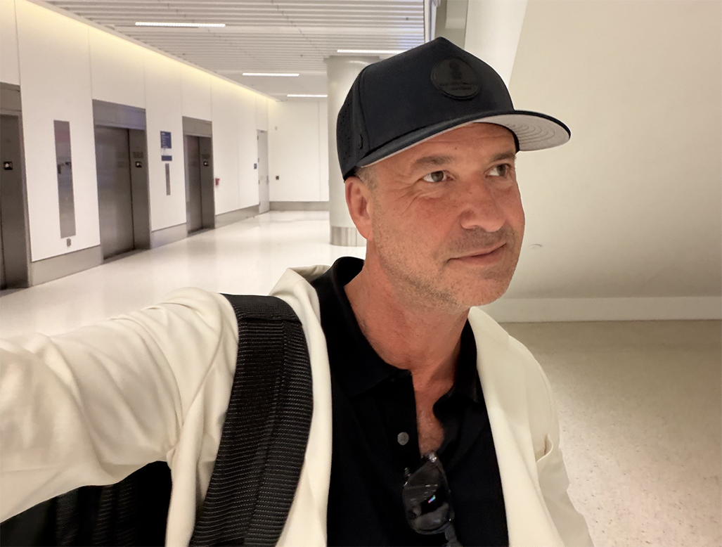 Rob Steven Williams in a cap and jacket with a backpack in an airport terminal